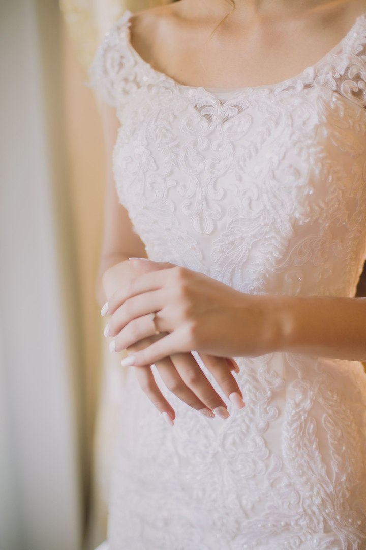 A bride's hand resting on her lace gown, showing her wedding ring