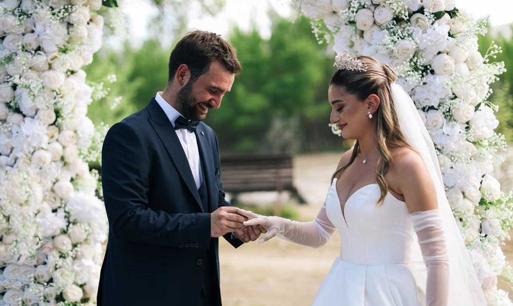 A bride and groom exchanging rings beneath a white floral arch