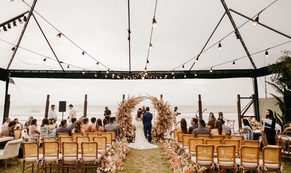 A wedding ceremony set up under string lights beside the sea