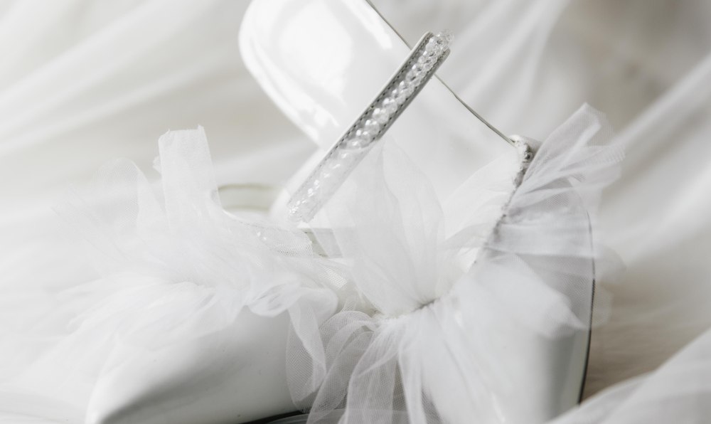 Delicate white bridal shoes with a tulle bow resting on a wedding dress