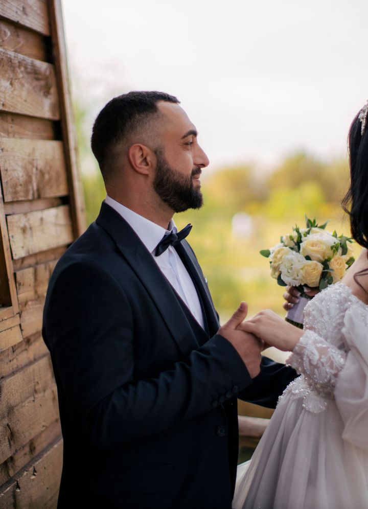 A groom and bride holding hands beside a wooden cabin window