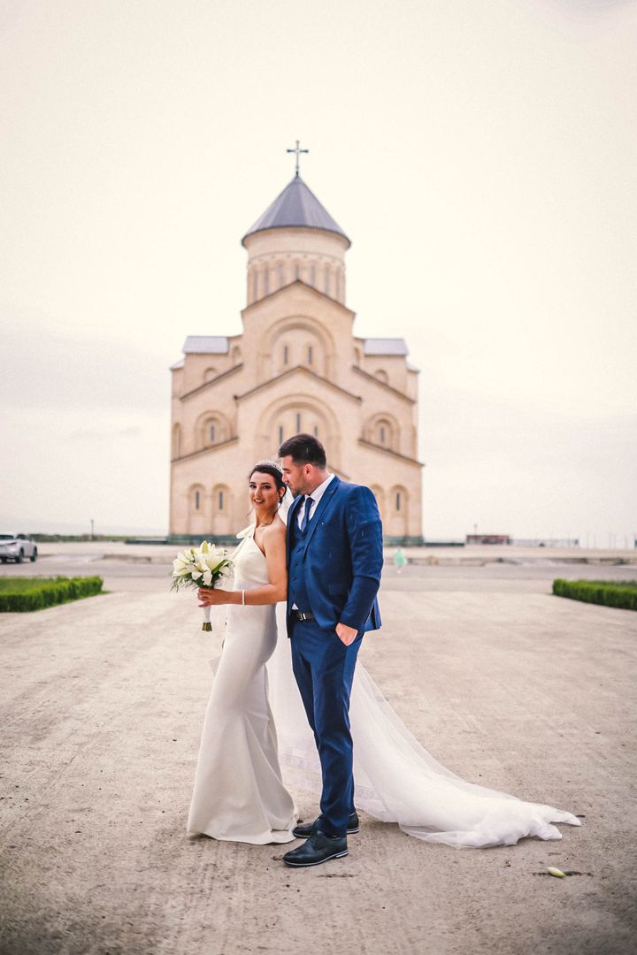 A bride and groom standing close in front of a Georgian church at sunset