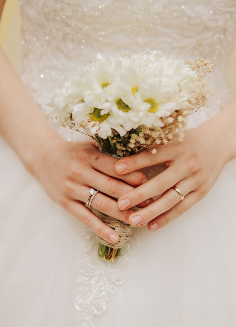 A bride holding a bouquet of white daisies against her wedding gown