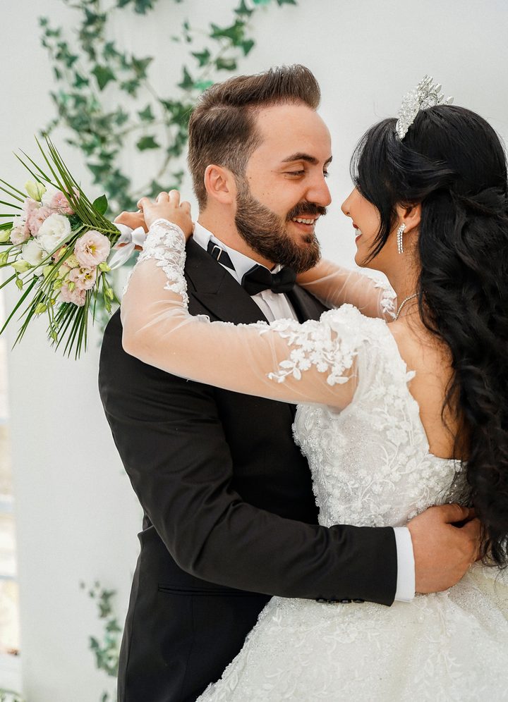 A groom and bride embracing and smiling, her hand resting on his shoulder