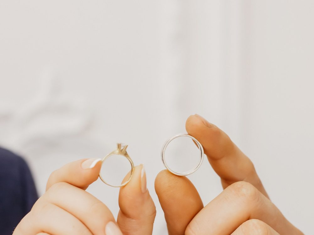 Two wedding rings held up between two sets of fingertips