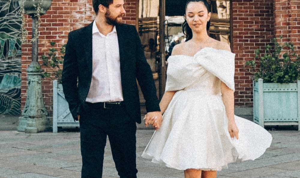 A bride and groom walking hand in hand through a brick archway entrance