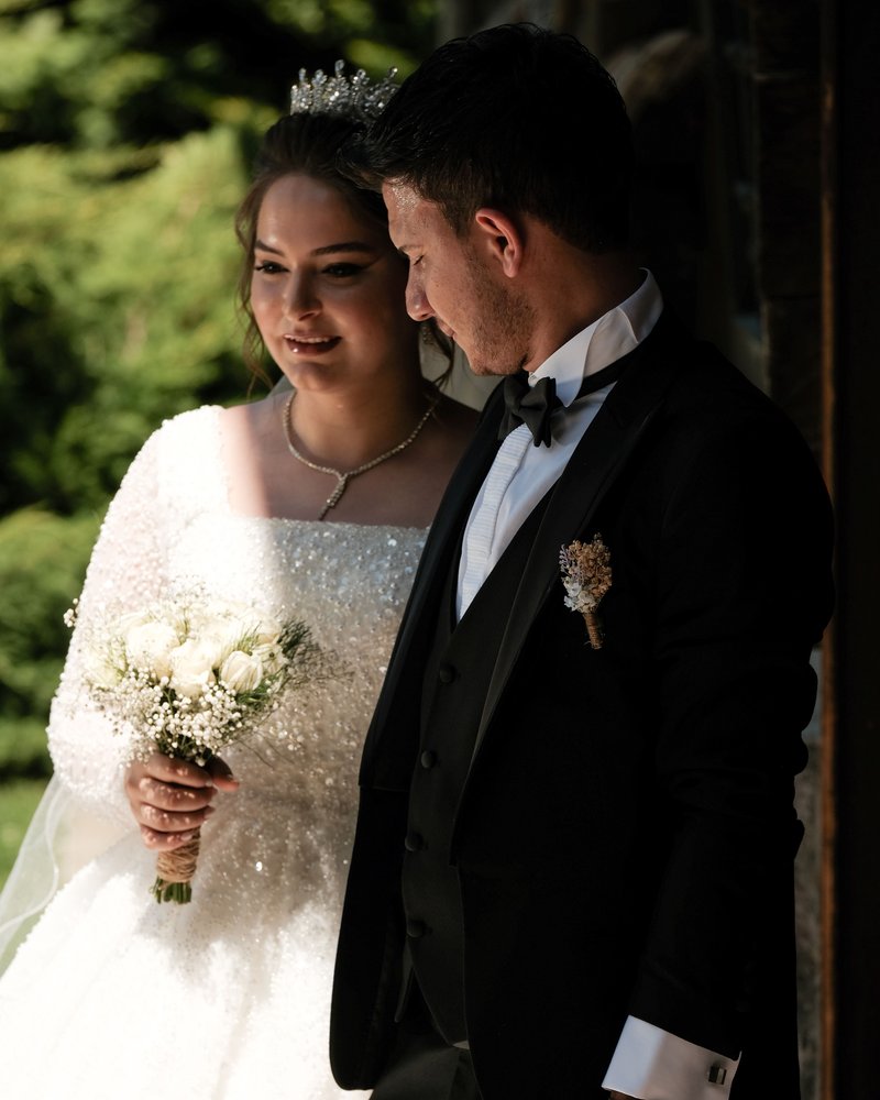 A bride and groom in formal wedding attire standing close together outdoors