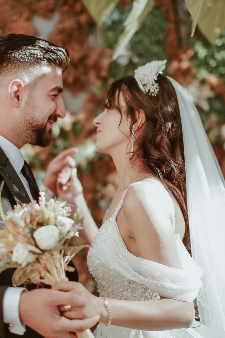 A bride and groom smiling closely at each other in a garden with autumn foliage