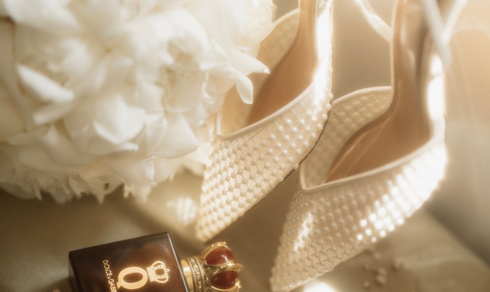 Wedding shoes, perfume and rings arranged beside a bridal bouquet