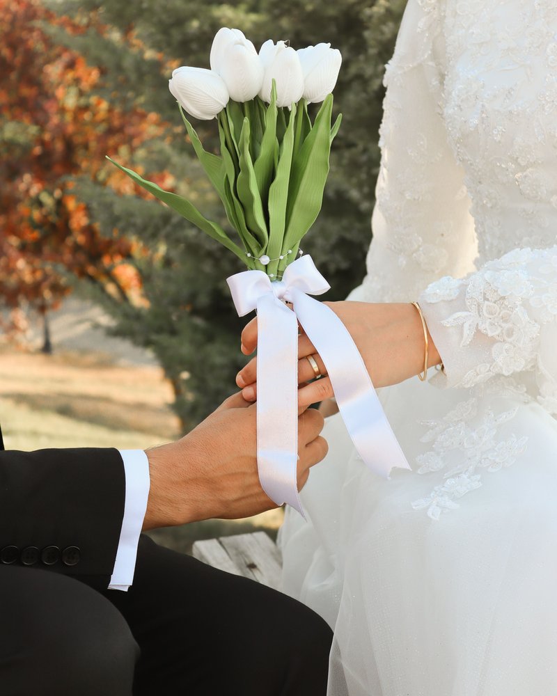 A groom handing a bouquet of white tulips to his bride