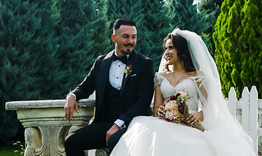 A bride and groom smiling at each other while seated on a garden bench