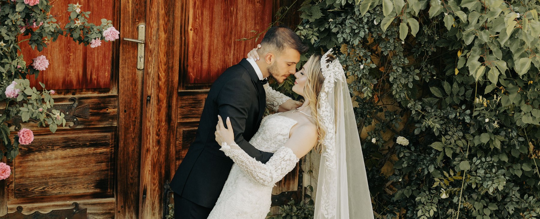 A bride and groom embracing in front of a rustic wooden door covered in climbing roses