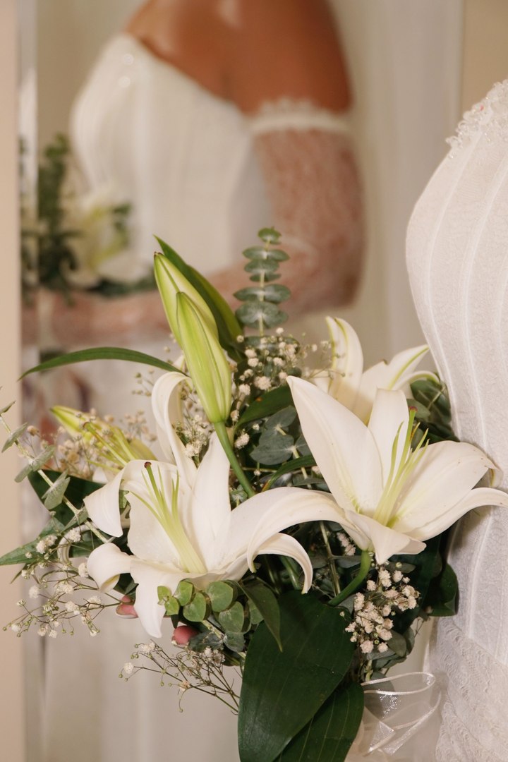 A bride holding a bouquet of white lilies against her lace gown