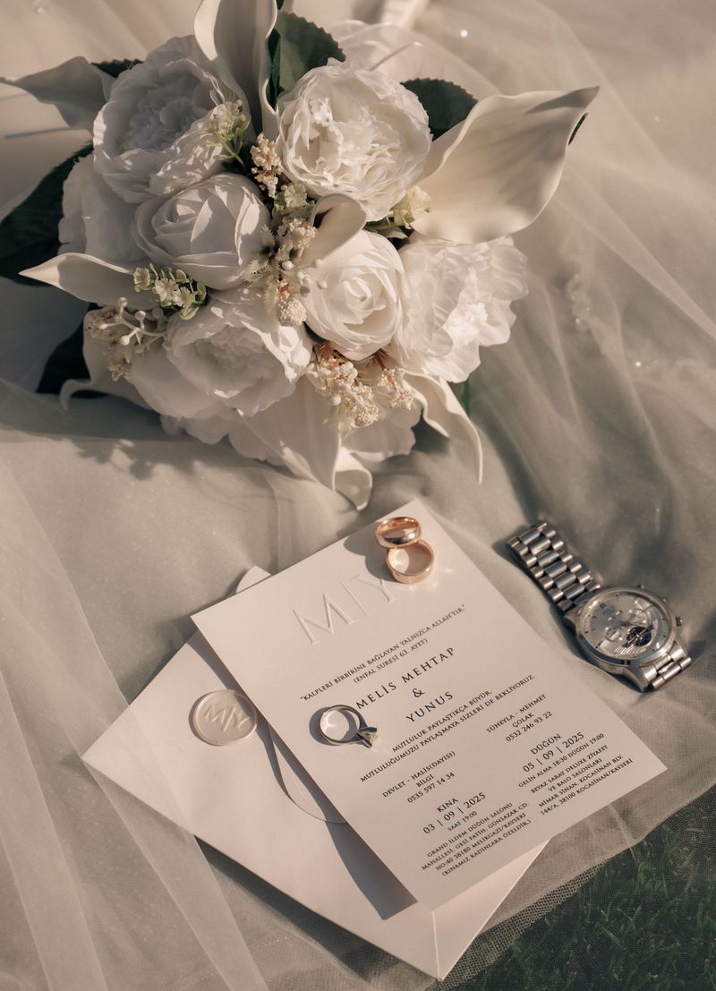 A wedding invitation, rings and a watch laid out on tulle fabric