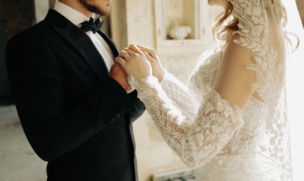 A groom in a tuxedo holding his bride's hand close together