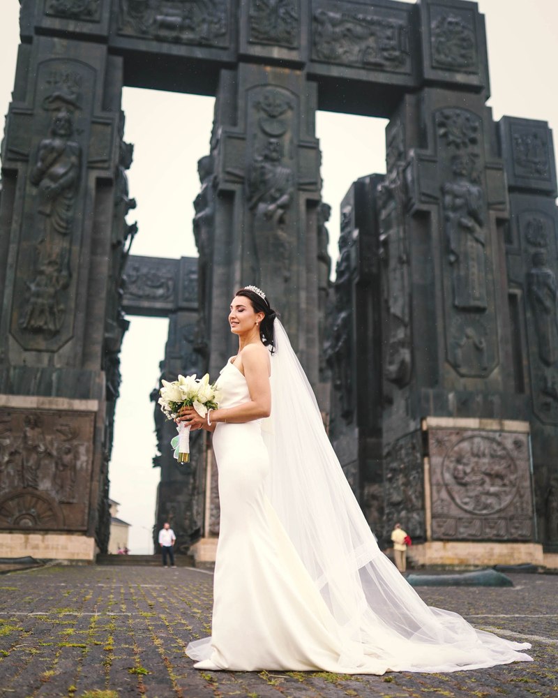 A bride in a veil standing before the towering stone pillars of a historic monument