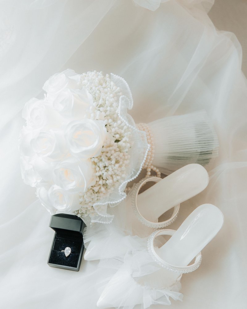 A bridal bouquet, veil and shoes laid out beside a ring box