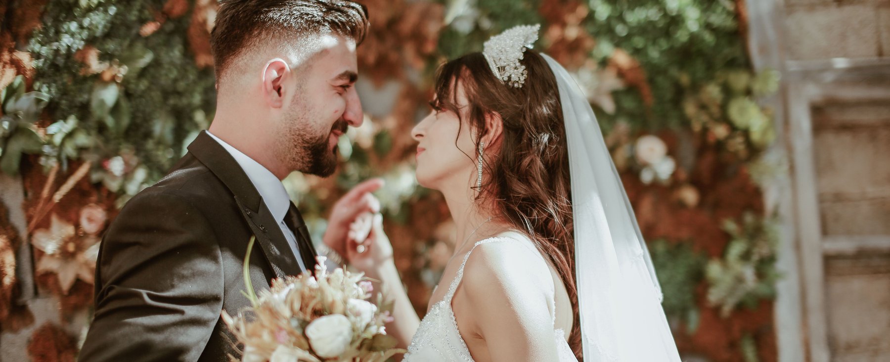 A bride and groom smiling closely at each other in a garden with autumn foliage