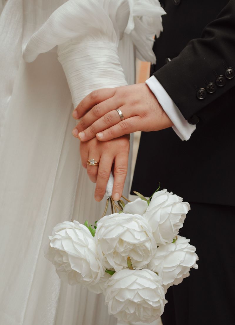 Close-up of a bride and groom's hands with wedding rings and a white bouquet