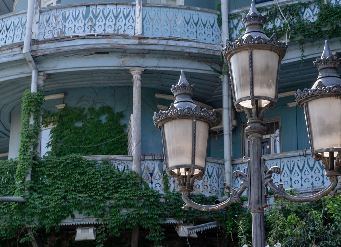 An ornate old Tbilisi balcony wrapped in greenery beside a vintage street lamp