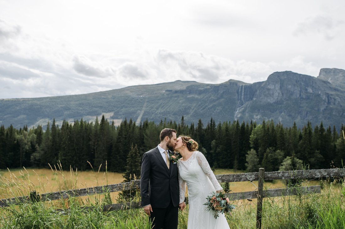 A couple in wedding attire kiss in front of the Georgian mountains
