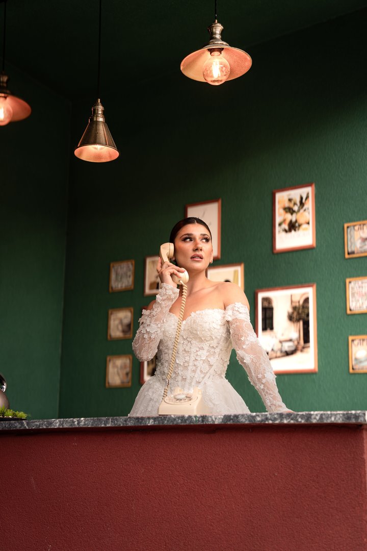 A bride in an off-the-shoulder lace gown takes a call over a red counter in Tbilisi