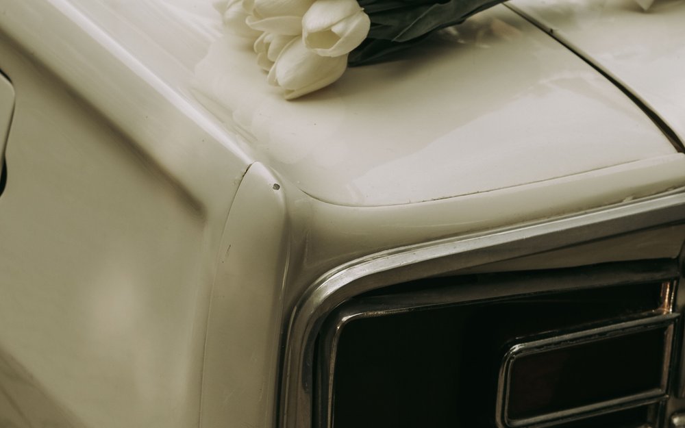 A bouquet of white tulips resting on the hood of a vintage wedding car