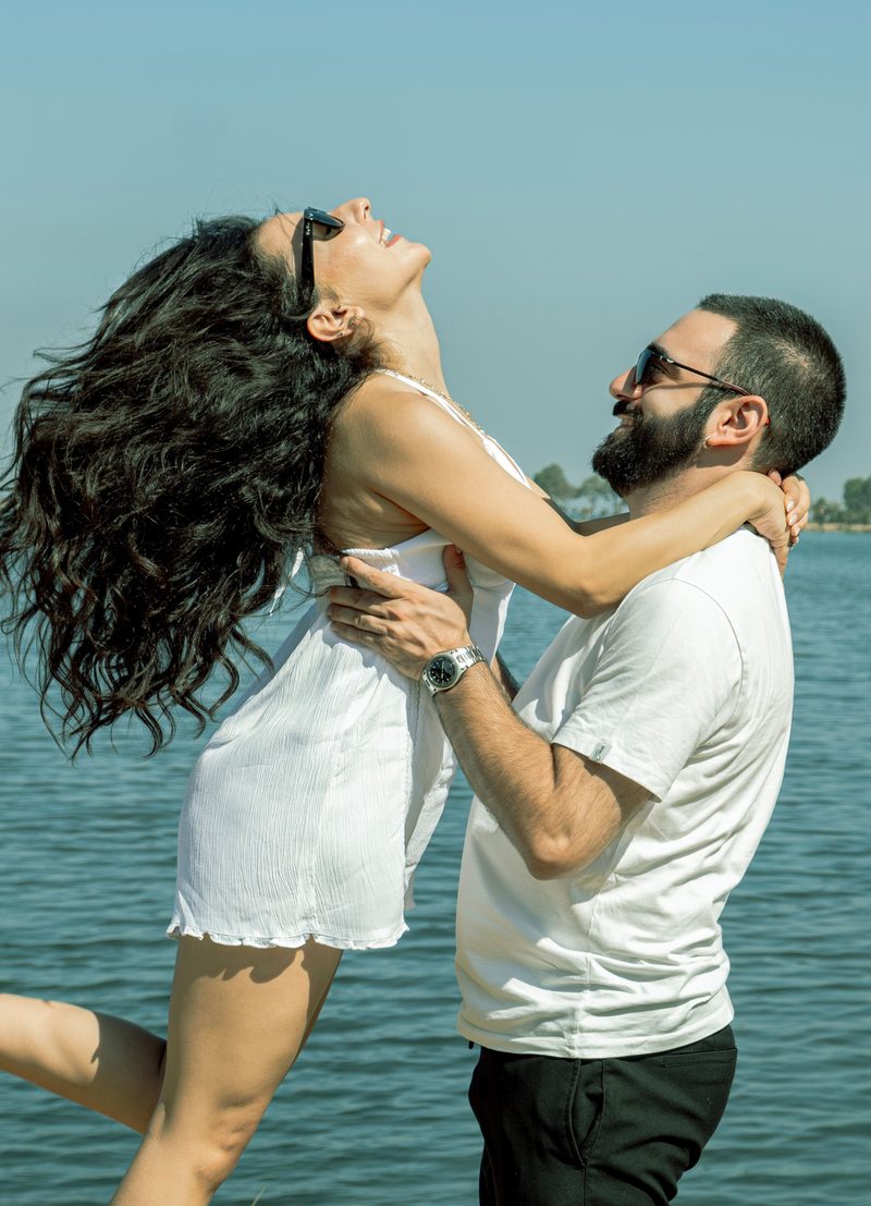 A joyful couple laughing and embracing by the water on a sunny day