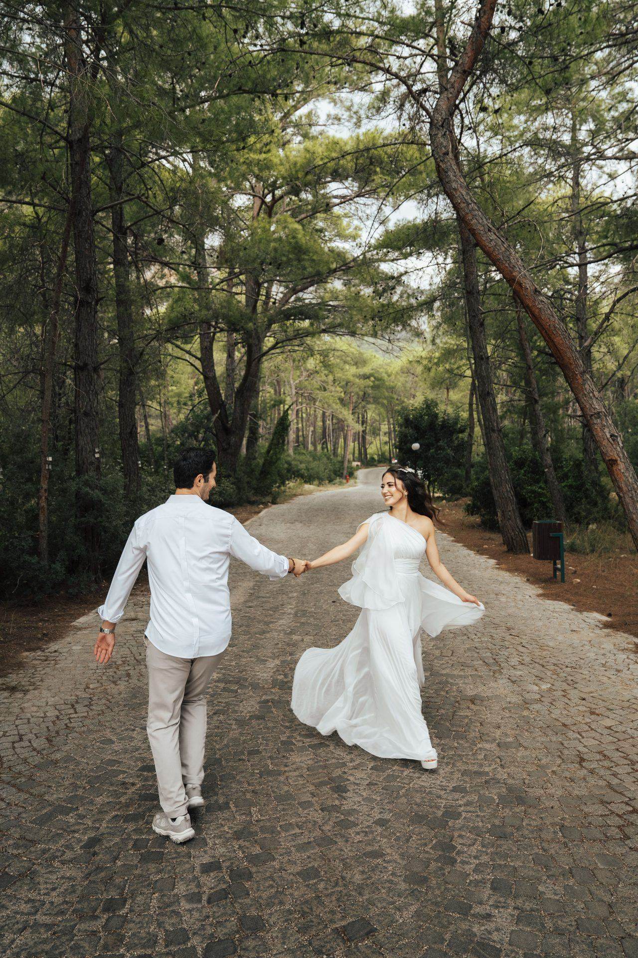 Newlywed couple walking hand in hand along a forest path