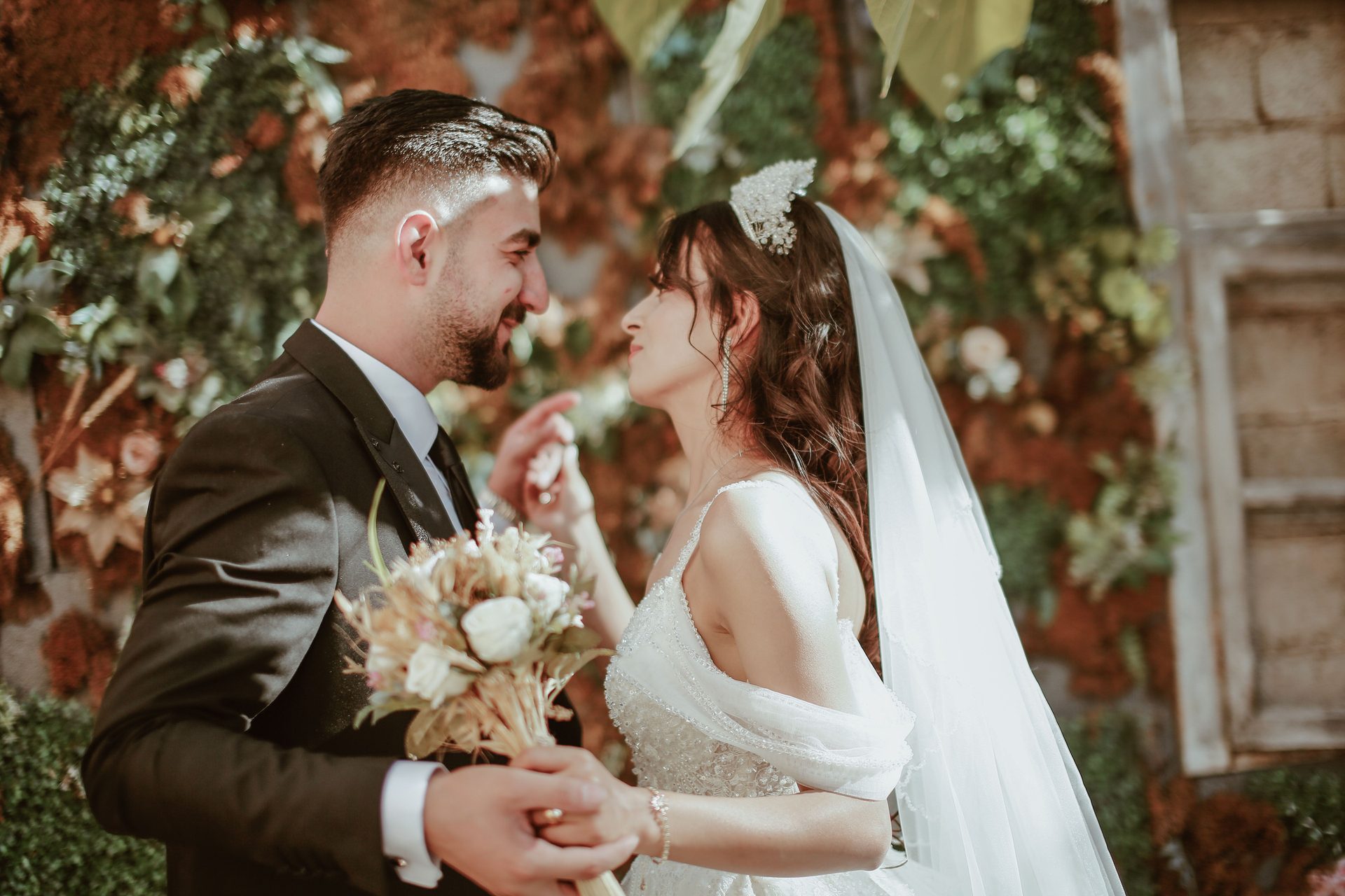 Bride and groom smiling at each other, holding a bouquet